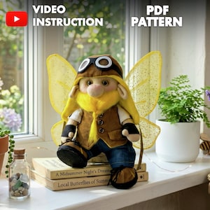 May include: A whimsical fairy doll with yellow wings, a brown aviator hat, and a yellow beard. The doll wears a brown vest, blue jeans, and black boots. The image includes the text "VIDEO INSTRUCTION" and "PDF PATTERN". The doll is sitting on books.