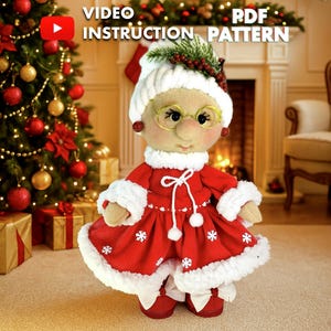 May include: A handmade Mrs. Claus doll in a red dress with white trim and snowflake accents. She wears a white hat, glasses, and a festive berry and greenery accent. The image includes text that reads "VIDEO INSTRUCTION PATTERN PDF".