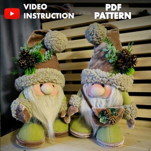 Puede incluir: Dos figuras de gnomos de peluche con largas barbas blancas, mejillas rosadas y atuendos verdes y marrones. Cada gnomo lleva un sombrero marrón alto con un ribete esponjoso y un acento decorativo de piñas y vegetación. La imagen incluye el texto "VIDEO INSTRUCTION" y "PDF PATTERN".
