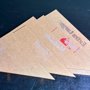 K&ouml;nnte beinhalten: Drei dreieckige St&uuml;cke aus transparentem Acryl mit aufgedrucktem Text. Die St&uuml;cke sind mit &bdquo;Small&ldquo;, &bdquo;Medium&ldquo; und &bdquo;Extra Large&ldquo; beschriftet. Die St&uuml;cke &bdquo;Medium&ldquo; und &bdquo;Extra Large&ldquo; haben ein rotes Logo.