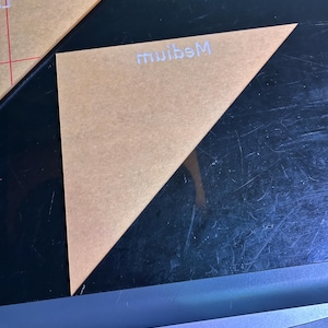 K&ouml;nnte beinhalten: Eine transparente, dreieckige Acrylschablone mit dem wei&szlig;en Schriftzug "Medium". Die Schablone ist beige und hat eine diagonale Linie. Sie wird f&uuml;r Bastelarbeiten und Design verwendet.