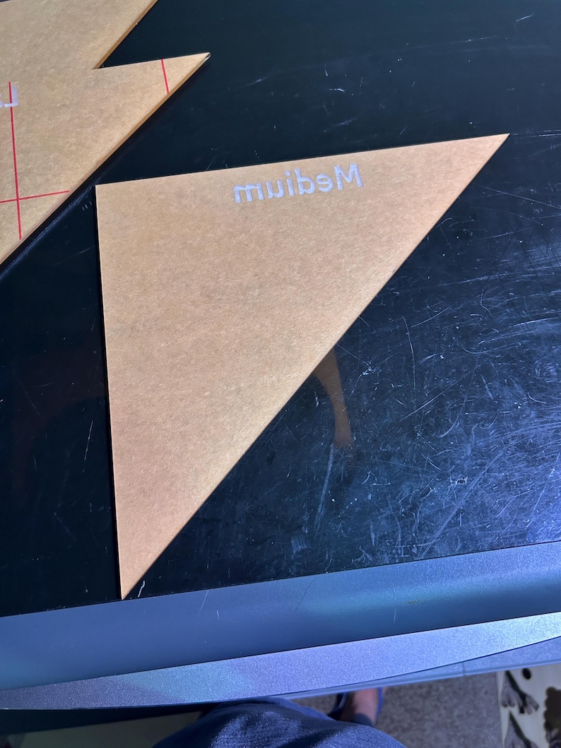 K&ouml;nnte beinhalten: Eine transparente, dreieckige Acrylschablone mit dem wei&szlig;en Schriftzug "Medium". Die Schablone ist beige und hat eine diagonale Linie. Sie wird f&uuml;r Bastelarbeiten und Design verwendet.