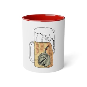 Puede incluir: Taza de cerámica blanca con interior rojo, con una ilustración de dibujos animados de una jarra de cerveza desbordante de espuma. La jarra tiene un asa y un emblema decorativo.