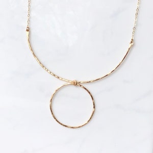May include: A gold necklace with a hammered circle pendant and a curved bar design. The necklace is made of a delicate chain.