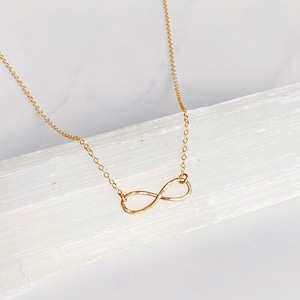 May include: A gold infinity necklace with a delicate chain. The infinity symbol is hammered for a textured look.