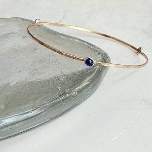 May include: A white ceramic mug with a black handle and the text "But First, Coffee" in a bold, black font. The mug is set against a blurred background, suggesting a cosy setting.