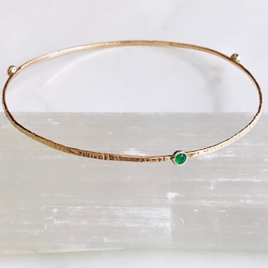 May include: A gold bangle bracelet with a textured finish and a single green gemstone.