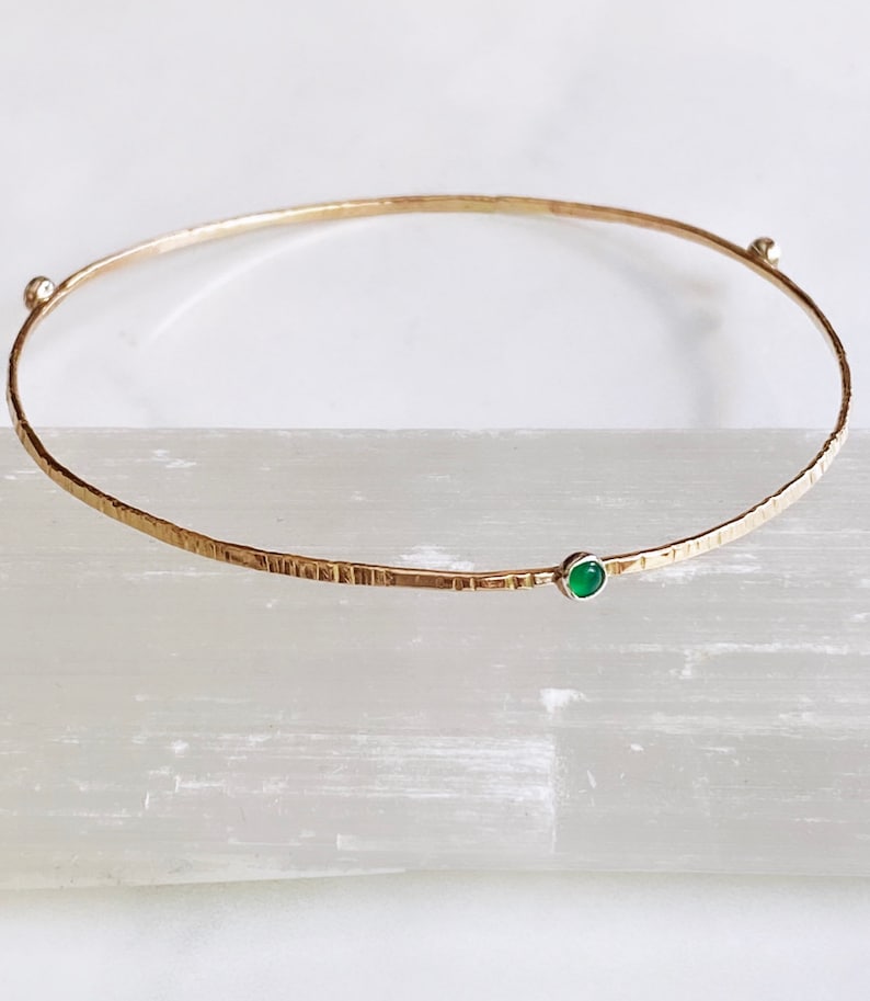 May include: A gold bangle bracelet with a textured finish and a single green gemstone.