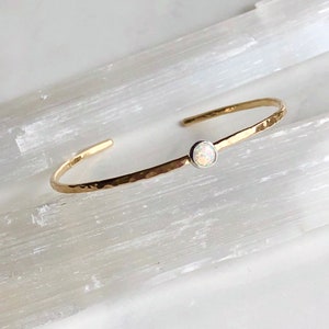 May include: A delicate gold hammered bangle bracelet with a single white opal gemstone set in a silver bezel.