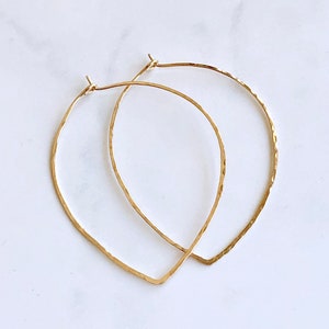 May include: A pair of gold-toned hammered metal hoop earrings with a teardrop shape.