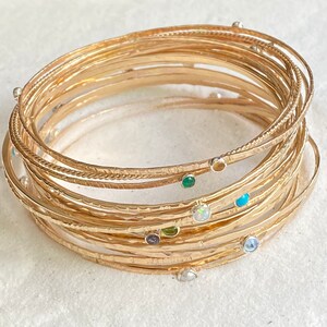 May include: A set of gold-toned bangle bracelets with various gemstones, including turquoise, opal, and emerald.