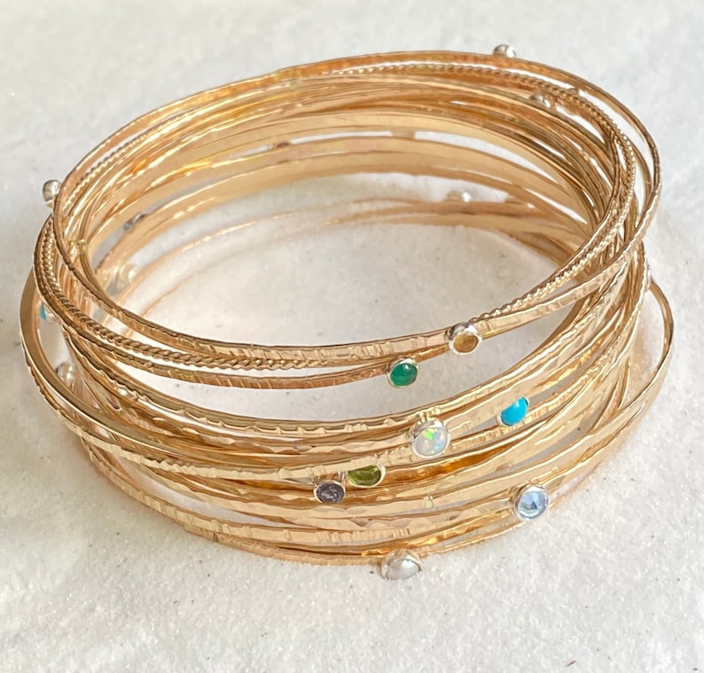 May include: A set of gold-toned bangle bracelets with various gemstones, including turquoise, opal, and emerald.