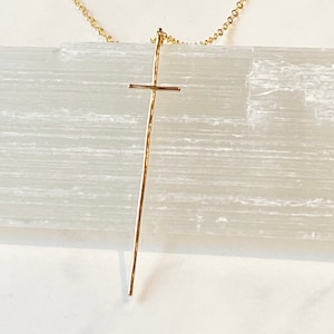Pode incluir: Um colar dourado com um pingente de cruz longo e fino.