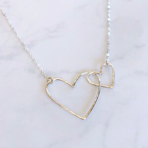 May include: A silver necklace featuring two interlocked heart pendants. The hearts are delicate and have a hammered finish.