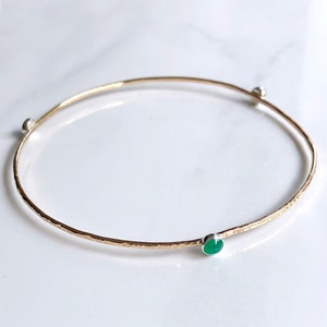 May include: A gold bangle bracelet with a hammered finish and a green gemstone accent.
