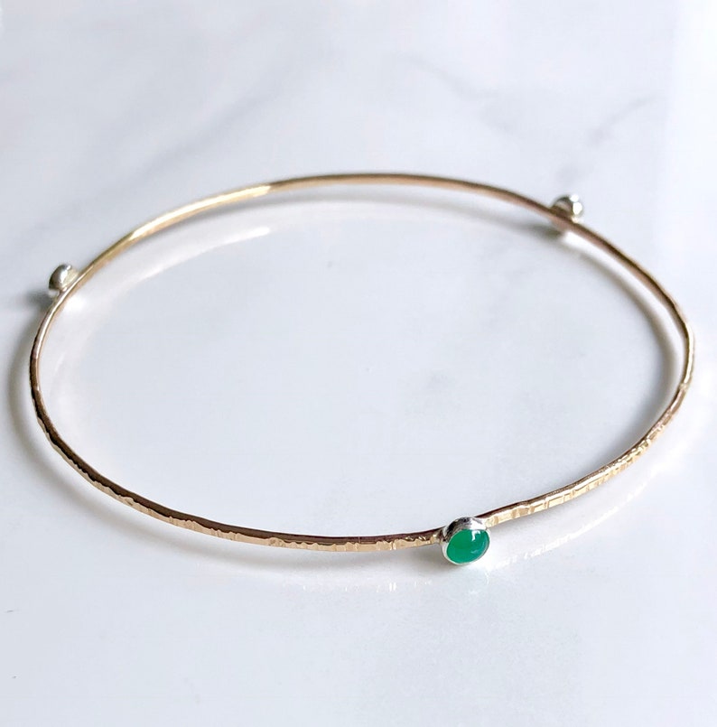May include: A gold bangle bracelet with a hammered finish and a green gemstone accent.