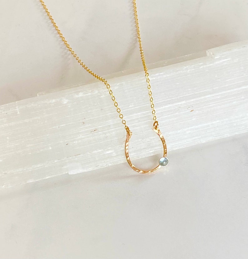 May include: A gold necklace with a hammered horseshoe pendant and a light blue gemstone.