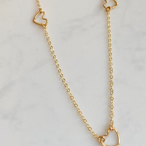 May include: A gold chain necklace with three delicate open heart charms.