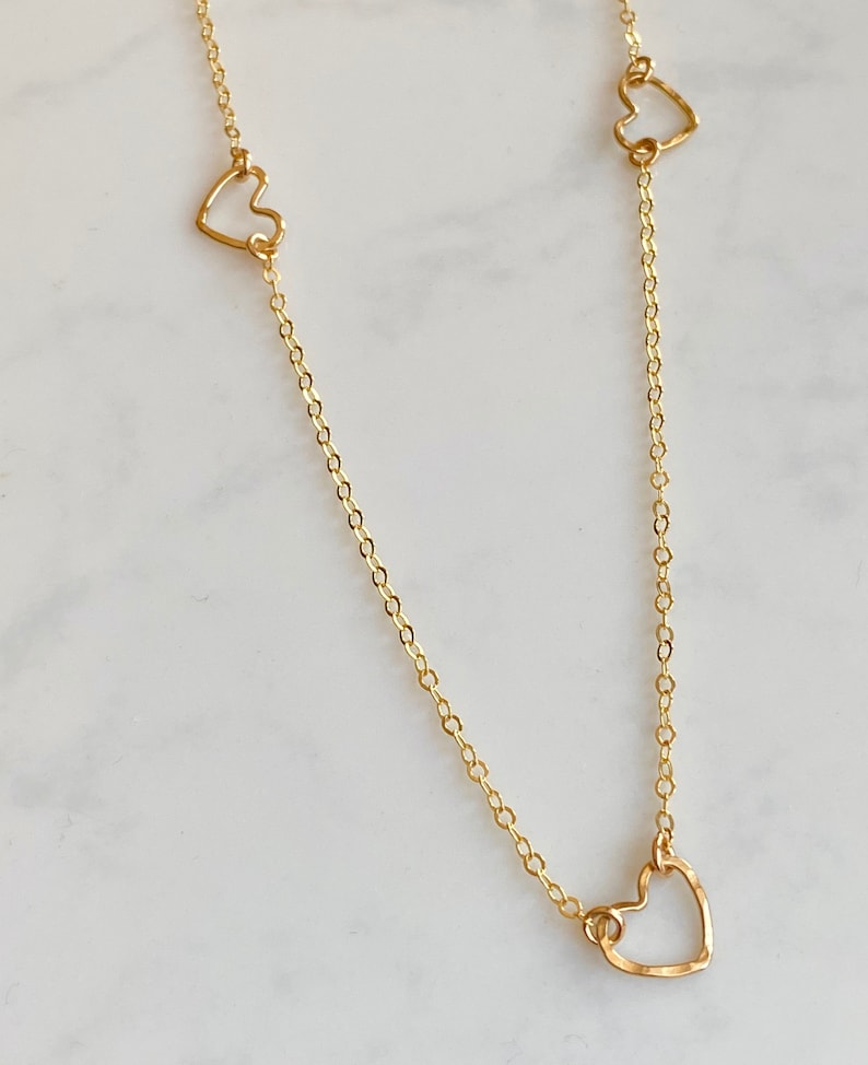 May include: A gold chain necklace with three delicate open heart charms.