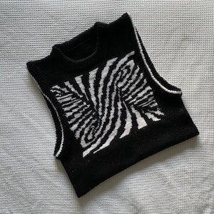 Pode incluir: Camisola preta sem mangas com um padrão de zebra branco e preto.