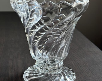 May include: A clear glass vase with a swirling, textured design. The vase has a wide, flared opening and a round base.