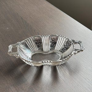 May include: A clear glass serving dish with silver-colored trim and two handles. The dish has a scalloped edge and a decorative design.