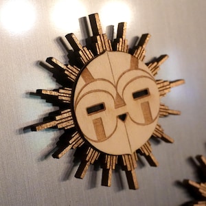 Peut inclure: Décoration en bois en forme de soleil avec un visage stylisé et des rayons. Le soleil a un visage brun clair avec des accents brun foncé et un contour brun foncé. Les rayons sont également brun foncé. Il s'agit probablement d'un aimant ou d'une décoration murale.