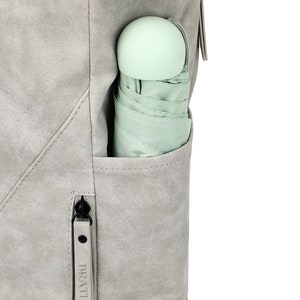 K&ouml;nnte beinhalten: Ein grauer Rucksack mit einer Rei&szlig;verschlusstasche an der Seite. Ein hellgr&uuml;ner Regenschirm ist in die Tasche gesteckt. Der Rei&szlig;verschluss hat den Schriftzug "BRAT" aufgedruckt.