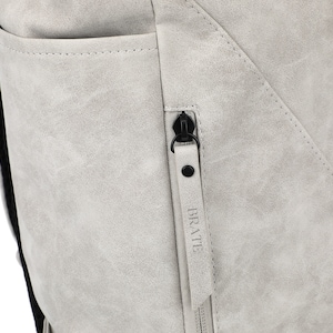 K&ouml;nnte beinhalten: Nahaufnahme eines grauen Rucksacks mit einem Rei&szlig;verschluss, der "BRATTE" sagt.