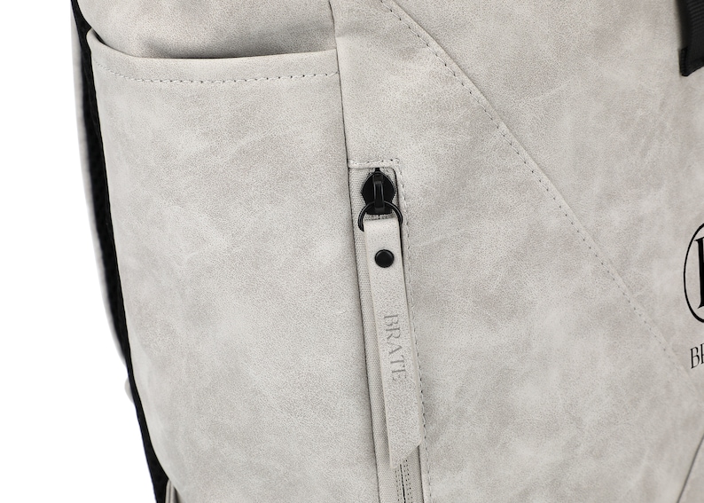 K&ouml;nnte beinhalten: Nahaufnahme eines grauen Rucksacks mit einem Rei&szlig;verschluss, der "BRATTE" sagt.