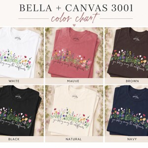 以下が含まれることがあります： 白、モーヴ、茶色、黒、ナチュラル、ネイビーの6色展開のBella + Canvas 3001 Tシャツのカラーチャート。各シャツには、テキスト「you belong among the wildflowers」と花の模様が施されています。