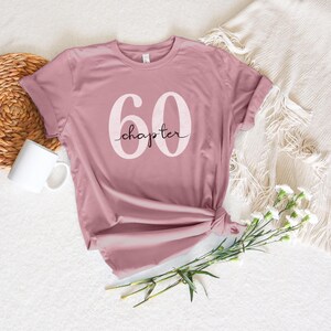 May include: A mauve t-shirt with the text "60 chapter" printed in white on the front.