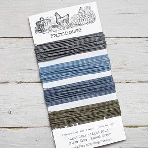 May include: A card with five spools of twine in different colors: light gray, light blue, slate blue, and khaki green. The card has the word "Farmhouse" printed on it and the text "Cras ord va ted ine: I read yazia eas col Light Gray Light Blue. Slate Blue Khaki Green www.Etsy.com/shop/UberArt".