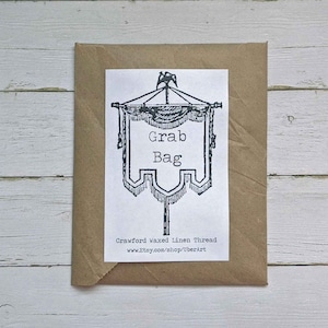 May include: A brown paper envelope with a white label that says "Grab Bag" and "Crawford Waxed Linen Thread" with a website address. The label has a black and white illustration of a banner with a crown on top.