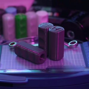 Puede incluir: Tres pomos de cambio impresos en 3D de color gris con un logotipo en blanco y negro en uno de los pomos.