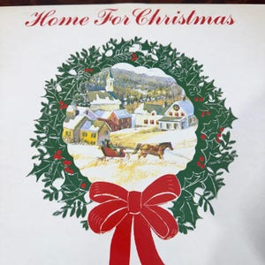 May include: A holiday-themed illustration with the text "Home For Christmas" in red. A green holly wreath frames a winter village scene with a horse-drawn sleigh and a large red bow at the bottom.
