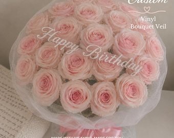 May include: A bouquet of light pink roses wrapped in a sheer white vinyl veil. The veil features the white text "Custom Vinyl Bouquet Veil" and "Happy Birthday" printed across the flowers. A pink satin ribbon is tied at the base of the bouquet.