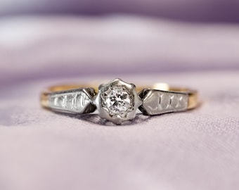 Puede incluir: Un anillo de compromiso vintage con un solo diamante redondo engastado en una banda de platino con un acento de oro amarillo.