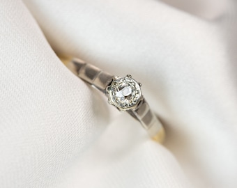 Puede incluir: Un anillo de plata con un solo diamante redondo engastado en garras. El anillo está sobre un fondo de tela blanca.