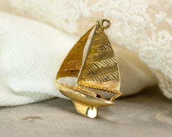 May include: A gold-colored sailboat brooch with textured sails and hull. The brooch features a detailed design, including a mast and decorative elements. The sailboat is set against a soft, neutral background, highlighting its intricate craftsmanship.