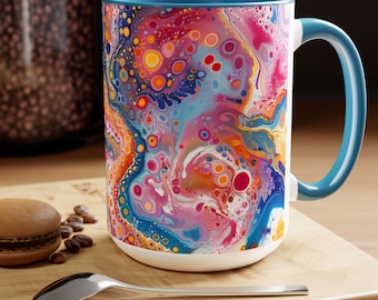 May include: A large, white ceramic mug with a blue rim and handle. The mug features a colorful abstract design with swirls of pink, blue, orange, and yellow, and small white, red, and orange circles throughout.