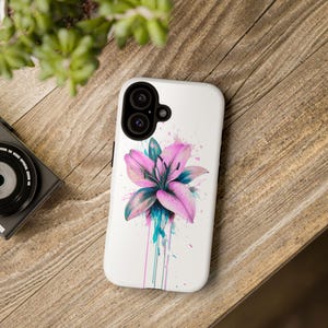 May include: White phone case with a watercolour design of a pink lily with teal and purple accents. The floral design has paint splatter effects. The phone case has a dual-lens camera cutout.