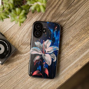 Puede incluir: Una funda de teléfono negra con un diseño de flor blanca y azul. La funda tiene un recorte para el objetivo de la cámara y un fondo negro.