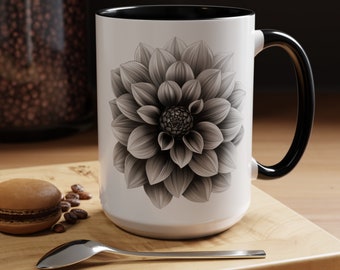 May include: A white ceramic mug with a black rim and handle features a black and white illustration of a large, detailed dahlia flower.