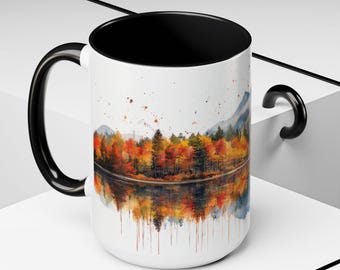 May include: White ceramic mug with a black handle and a black rim. The mug features a watercolor painting of a forest reflected in a lake. The trees are in shades of orange, yellow, and red, suggesting autumn.