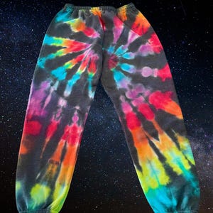 May include: Black sweatpants with a colorful tie-dye pattern in shades of pink, blue, green, yellow, and orange. The pattern is a spiral design.