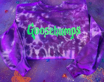 May include: Purple tie-dye sweatshirt with the word "Goosebumps" in green lettering.