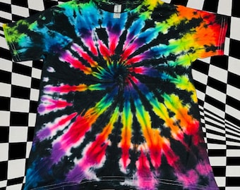 May include: A black tie-dye t-shirt with a spiral design. The shirt features a vibrant array of colors, including blue, green, yellow, orange, red, and purple, radiating from the center. The shirt is made of a soft material.