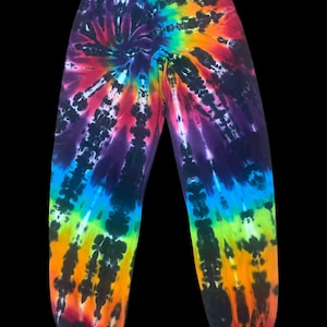 May include: Tie-dye sweatpants in a vibrant rainbow of colors, including purple, blue, green, yellow, orange, and red. The pants have an elastic waistband and cuffs, creating a comfortable and stylish look. The tie-dye pattern radiates from the center.