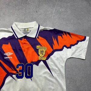 May include: White soccer jersey with orange and purple accents. Features the number 30 in blue, a Scottish Football Association emblem, and the Umbro logo. The jersey has a collared neckline and a geometric design.